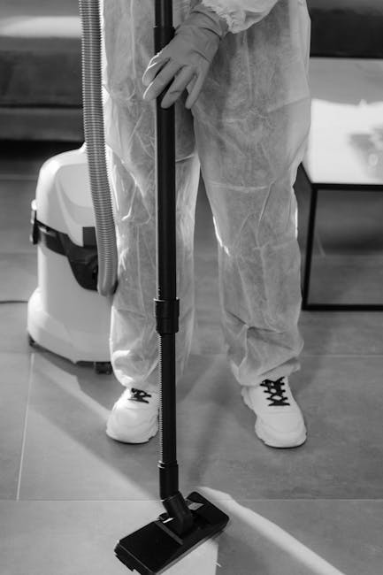 A person dressed in protective clothing and gloves is using a vacuum cleaner with a floor attachment to perform surface cleaning on a smooth, hard floor. The vacuum cleaner is positioned nearby, and the person is handling the cleaning equipment with both hands, indicating a thorough approach to deep cleaning or sanitisation in a commercial or residential space. The setting appears well-lit, emphasizing the cleanliness and maintained condition of the area. This image exemplifies professional cleaning practices, as offered by companies like Cleaners TW9, aligned with their Richmond Hill end of tenancy cleaning services, TW9.